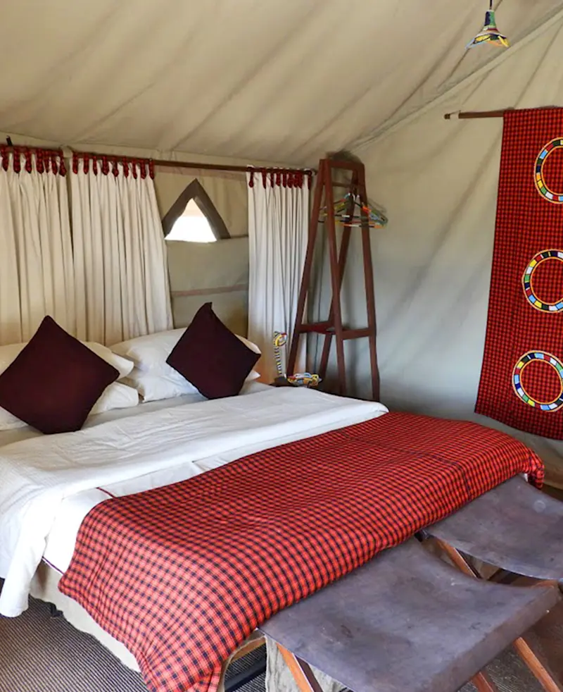Safari tent bedroom with a red plaid blanket, pillows, and a Maasai-patterned wall hanging