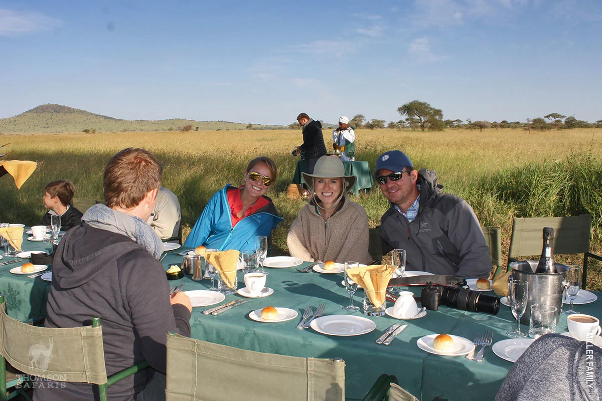 Travelers sharing breakfast at a table set out in the grassland