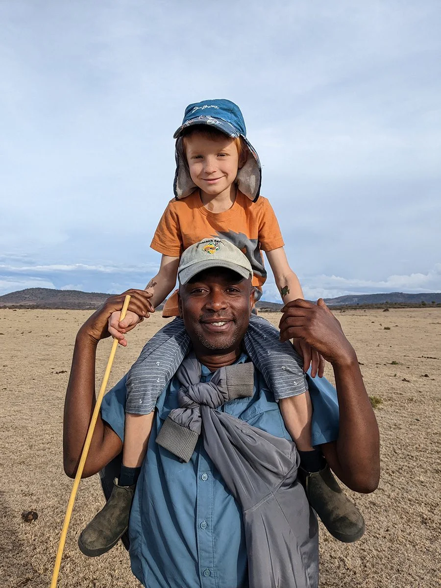 Smiling guide carrying a young boy on his shoulders on an open plain