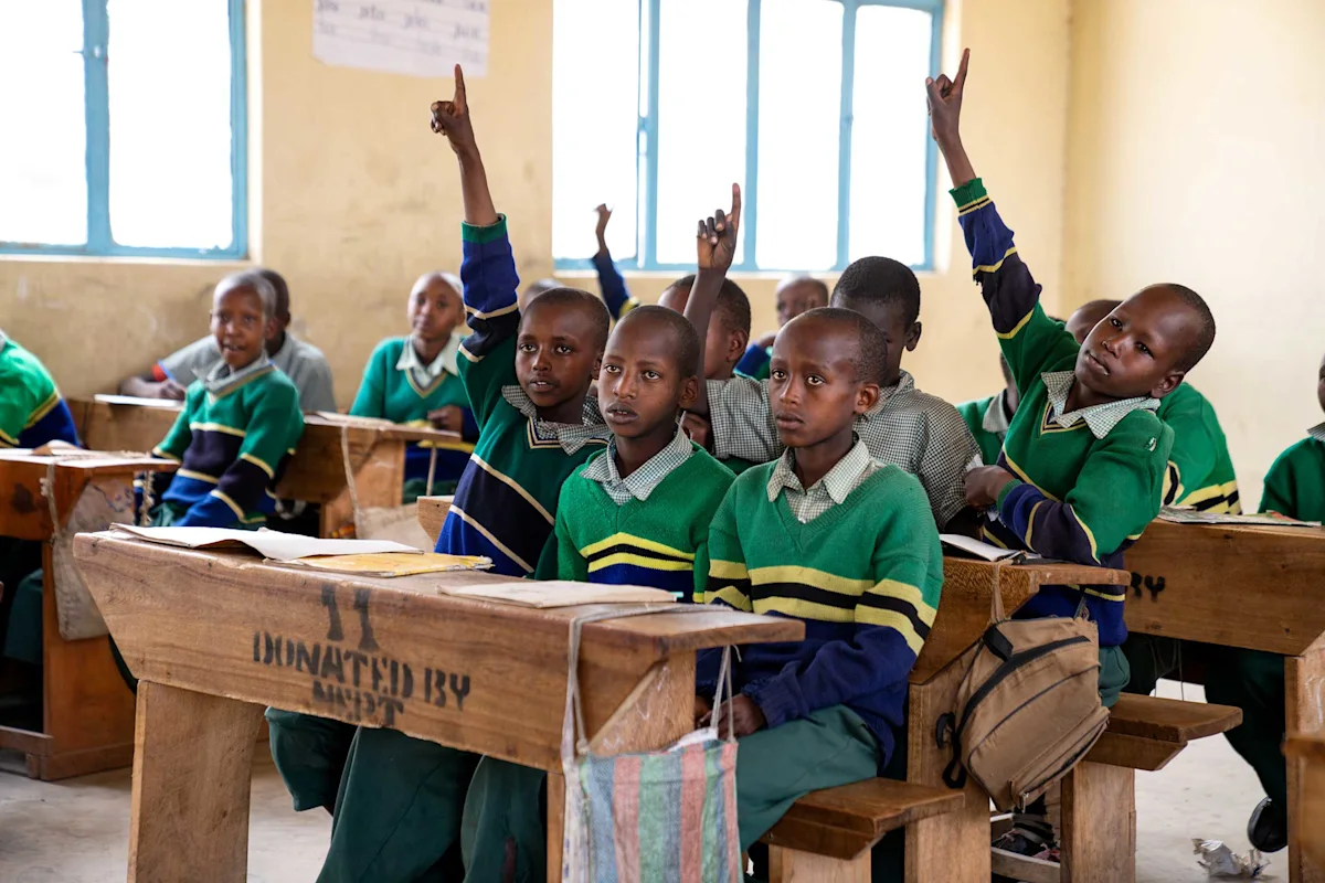 Uniformed students raising their hands at wooden desks in a classroom