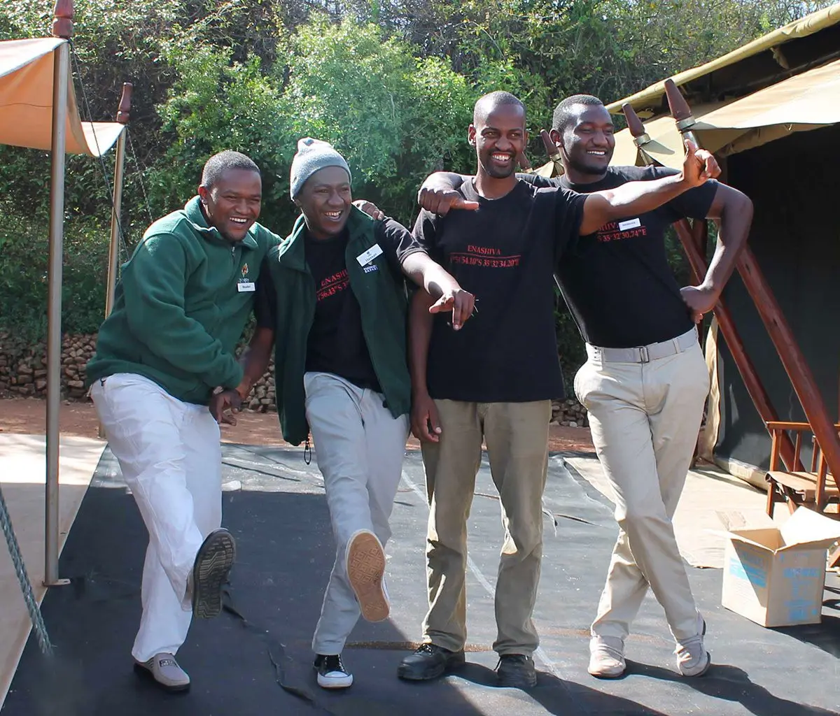 Four smiling camp staff posing playfully outside a tent in the Eastern Serengeti