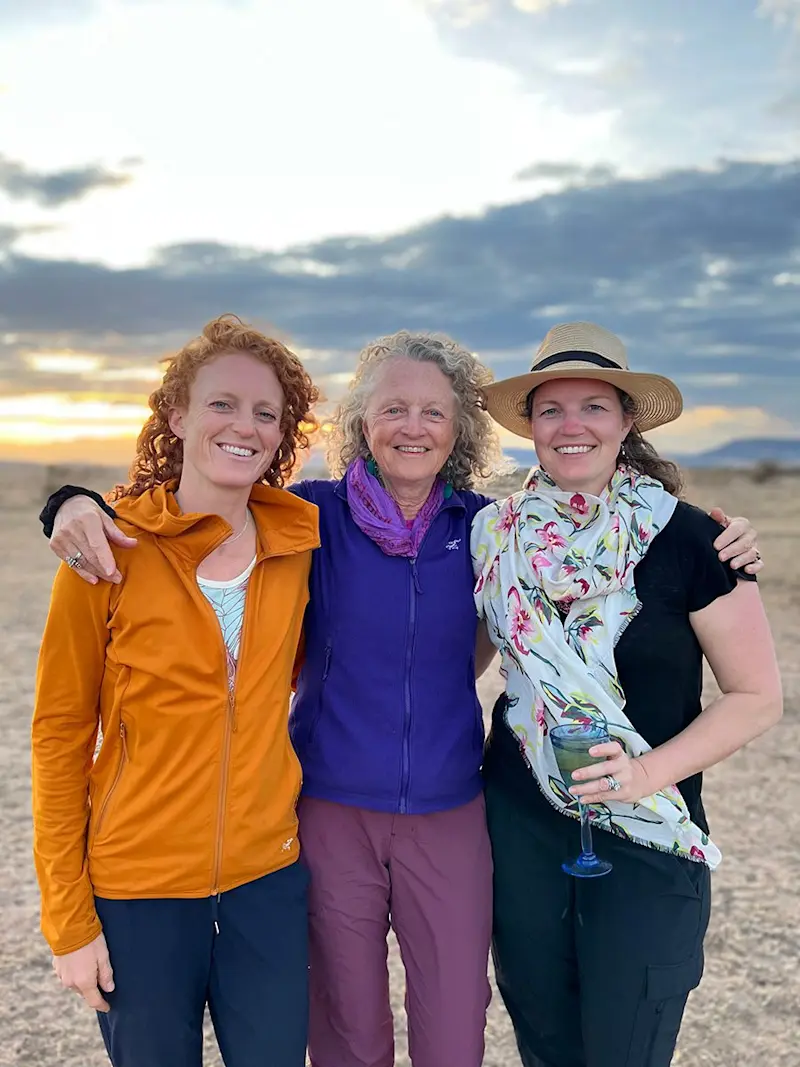 Three women smiling arm in arm on the savanna at sunset