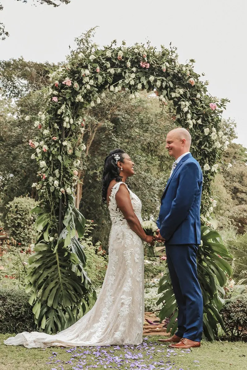 Bride and groom holding hands under a floral arch in a garden