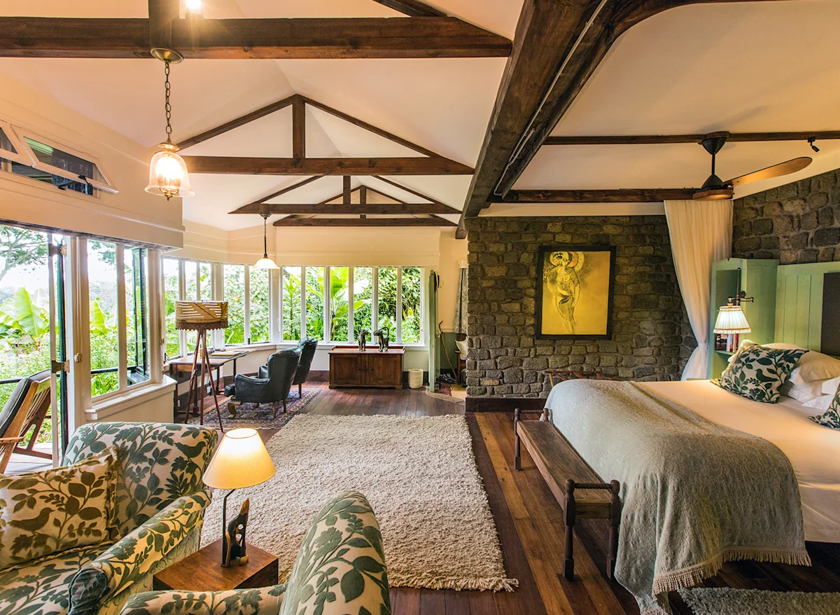 Cottage bedroom with stone fireplace wall, armchairs and large windows at Gibb's Farm