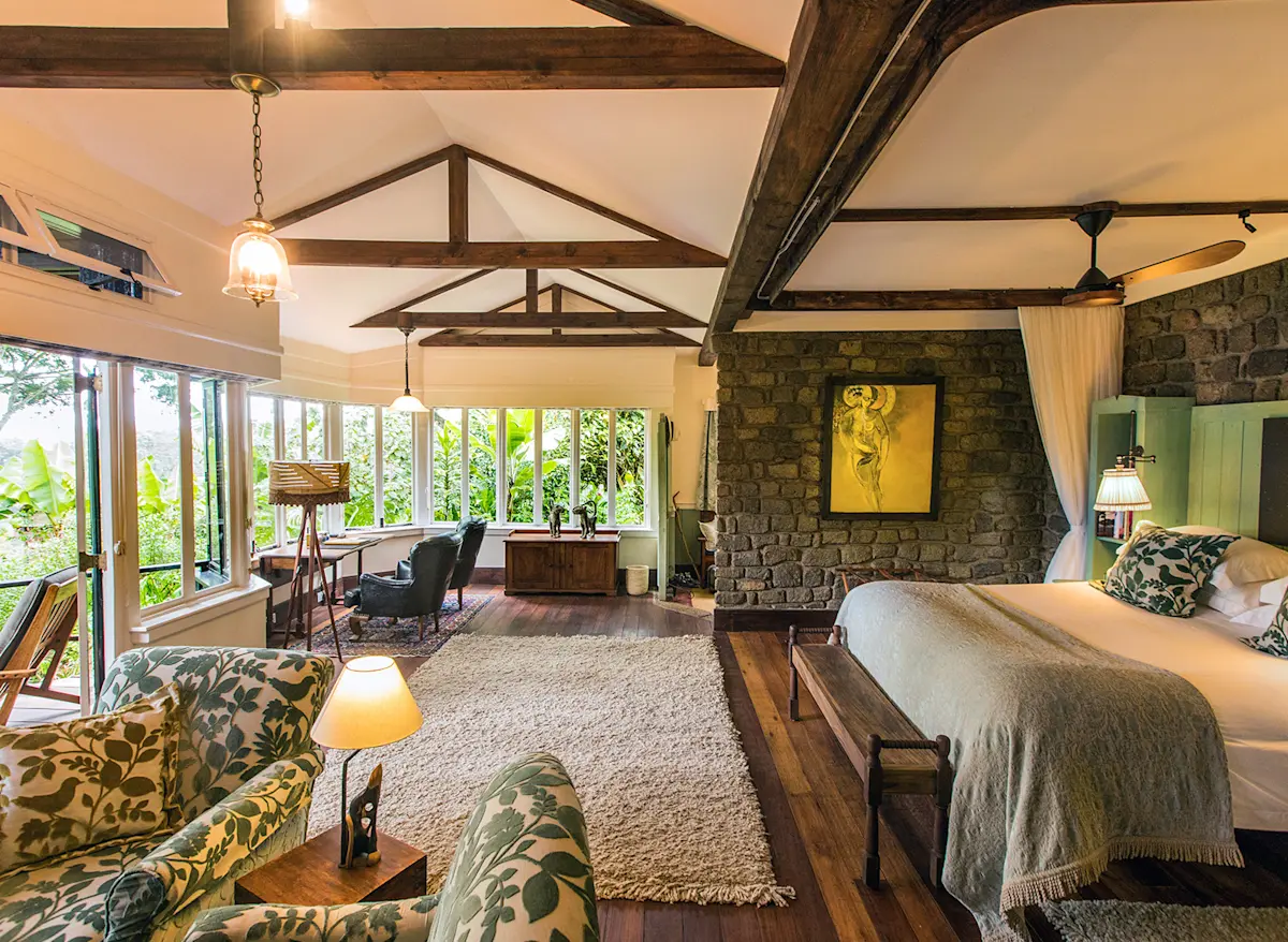 Cottage bedroom with stone fireplace wall, armchairs and large windows at Gibb's Farm
