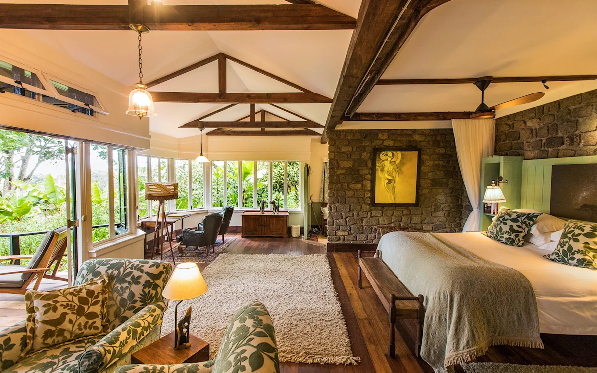 Cottage bedroom with stone fireplace wall, armchairs and large windows at Gibb's Farm