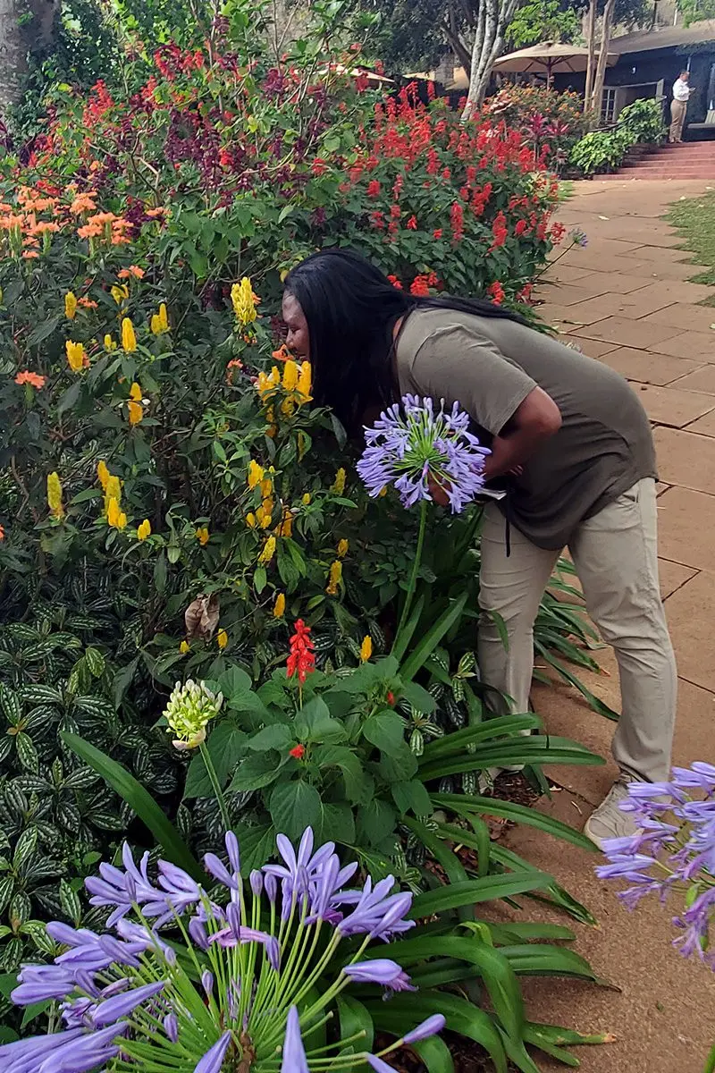 Woman leaning in to smell flowers along a garden path