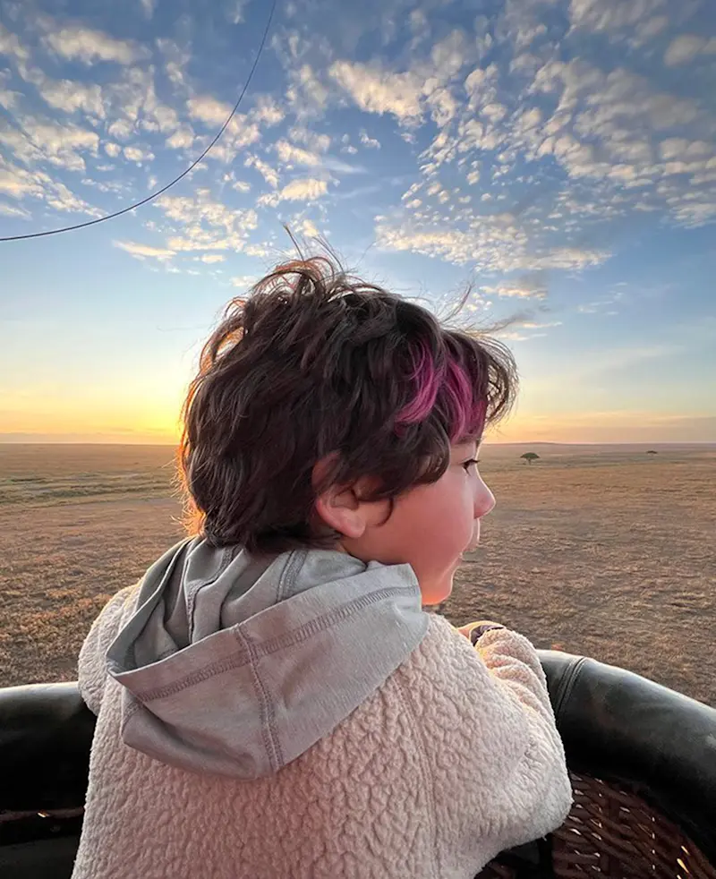 Child looking out from a hot air balloon basket over the plains at sunrise