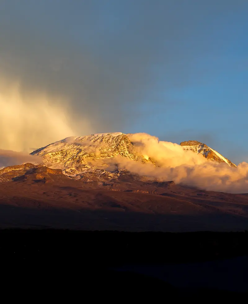 Snow-capped summit of Mount Kilimanjaro lit by golden light above the clouds