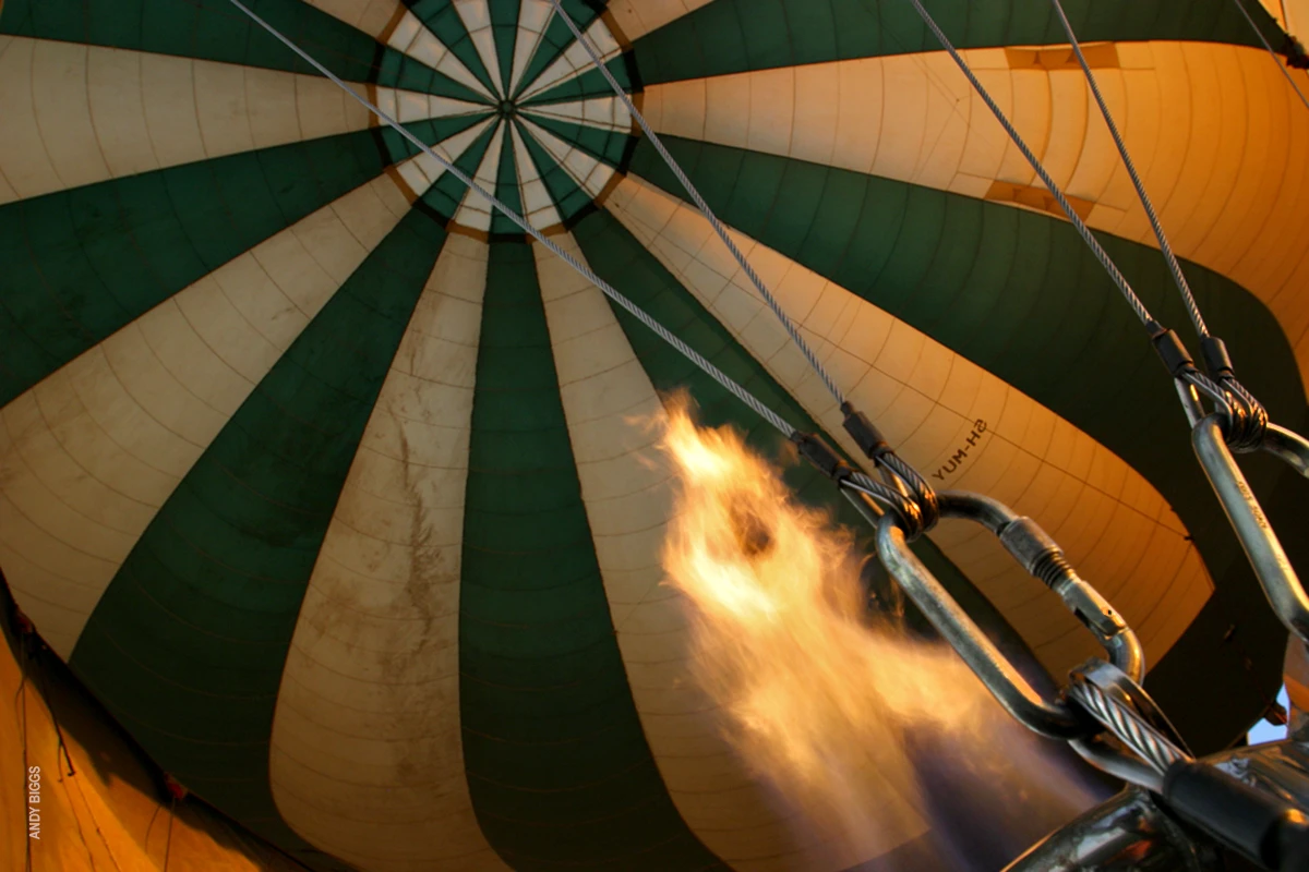 Burner flame firing inside a green and cream hot air balloon envelope