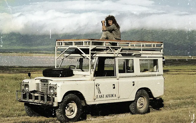 Vintage photo of Judi Wineland with a camera on the roof of a Land Rover beside a lake