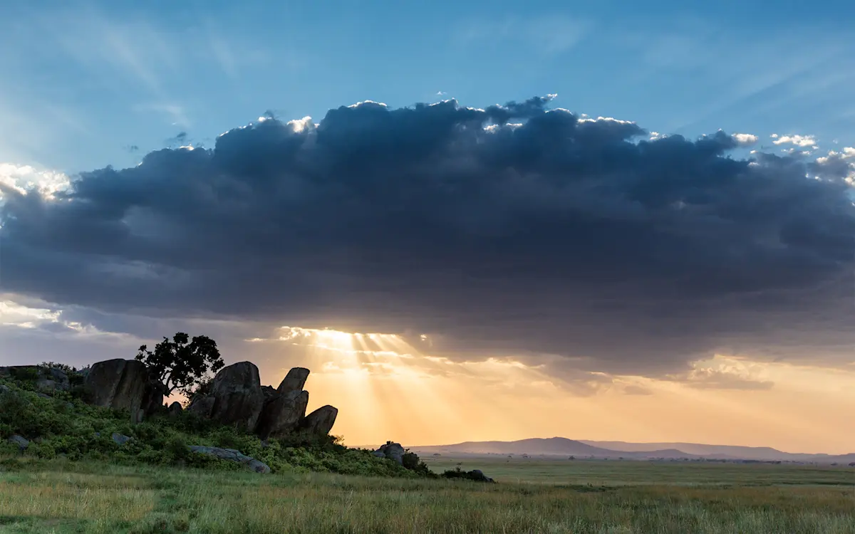 Sunbeams breaking through clouds over a rocky kopje on the Serengeti plains