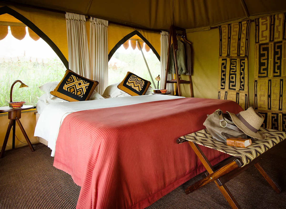 Double bed with red blanket and patterned pillows inside a Nyumba tent