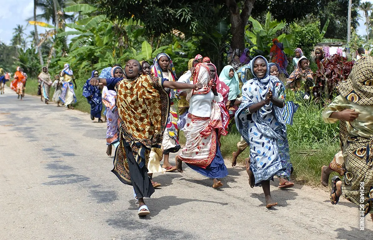 Women in colorful kangas running and laughing along a street in Zanzibar