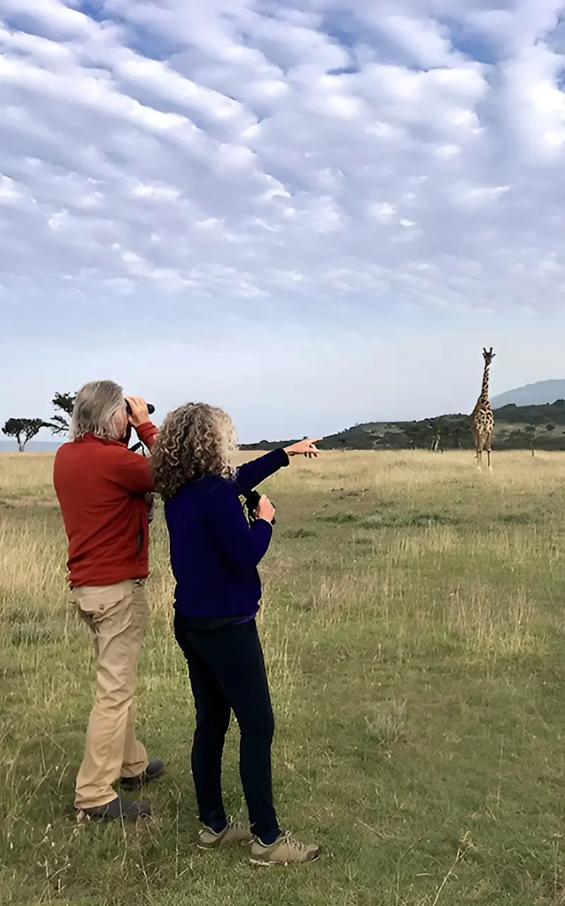 Rick Thomson and Judi Wineland looking through binoculars at a distant giraffe