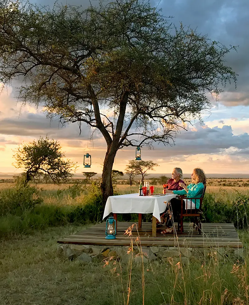 Rick Thomson and Judi Wineland dining at a table under an acacia tree at sunset