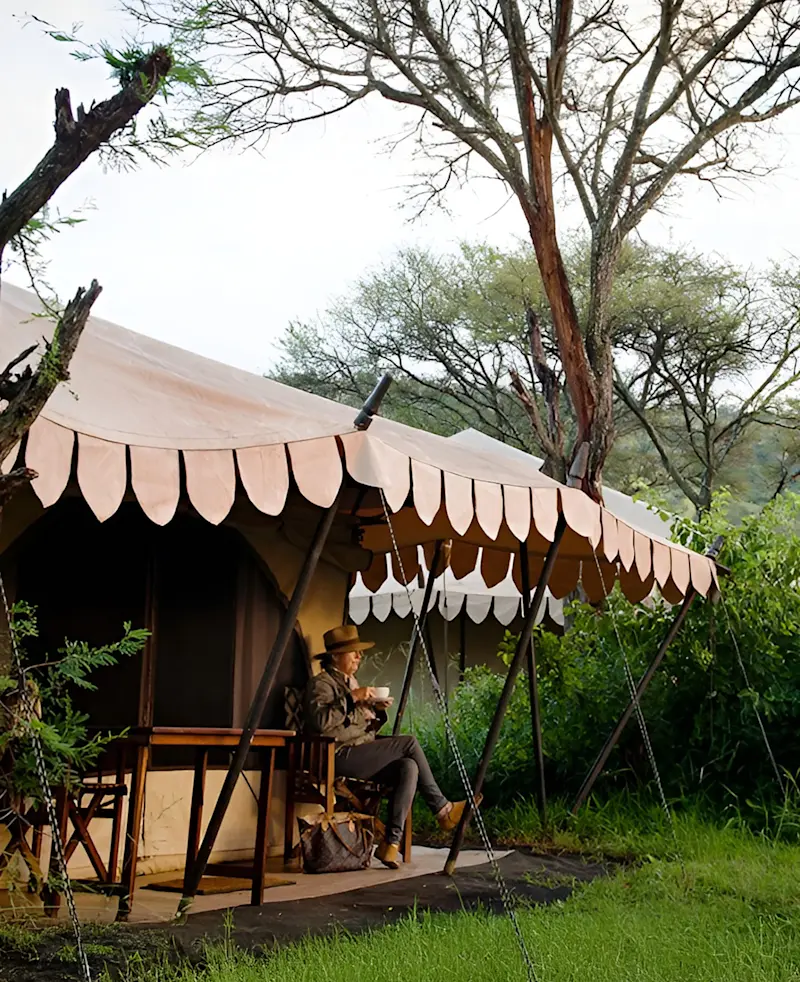 Guest relaxing on the porch of a canvas tent beneath trees