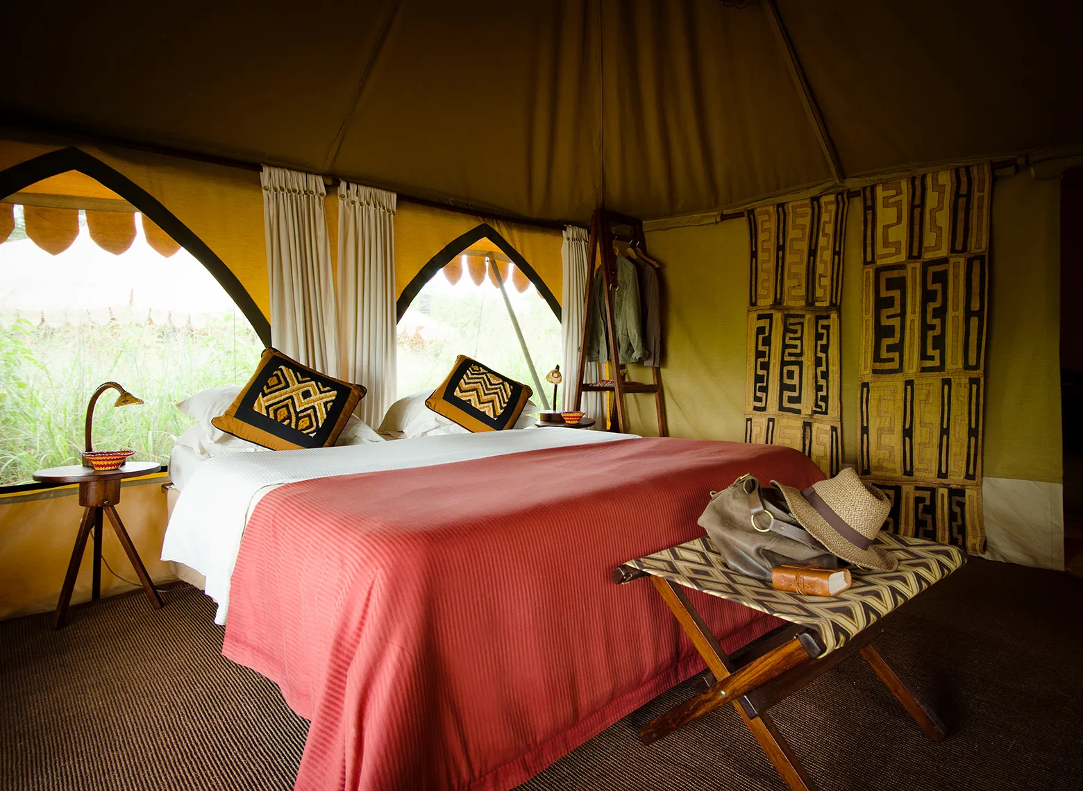 Double bed with red blanket and patterned pillows inside a tent at Central Serengeti Nyumba
