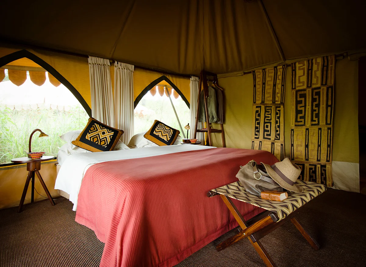 Double bed with red blanket and patterned pillows inside a tent at Central Serengeti Nyumba
