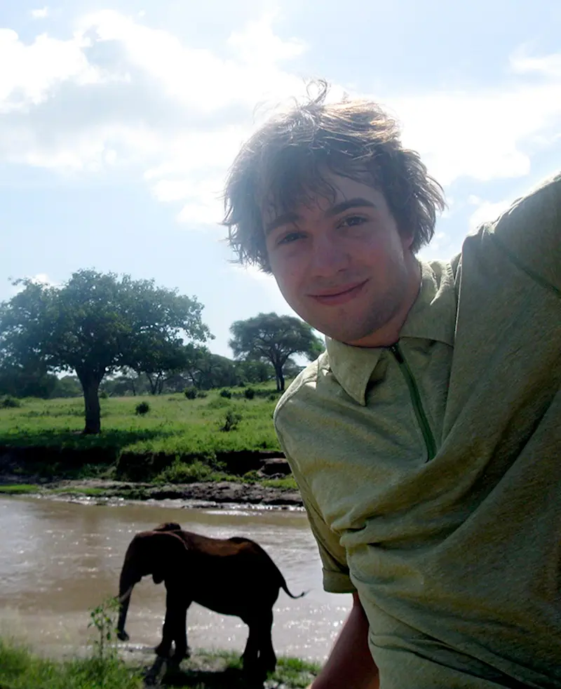 Smiling young man taking a selfie with an elephant at a river behind him