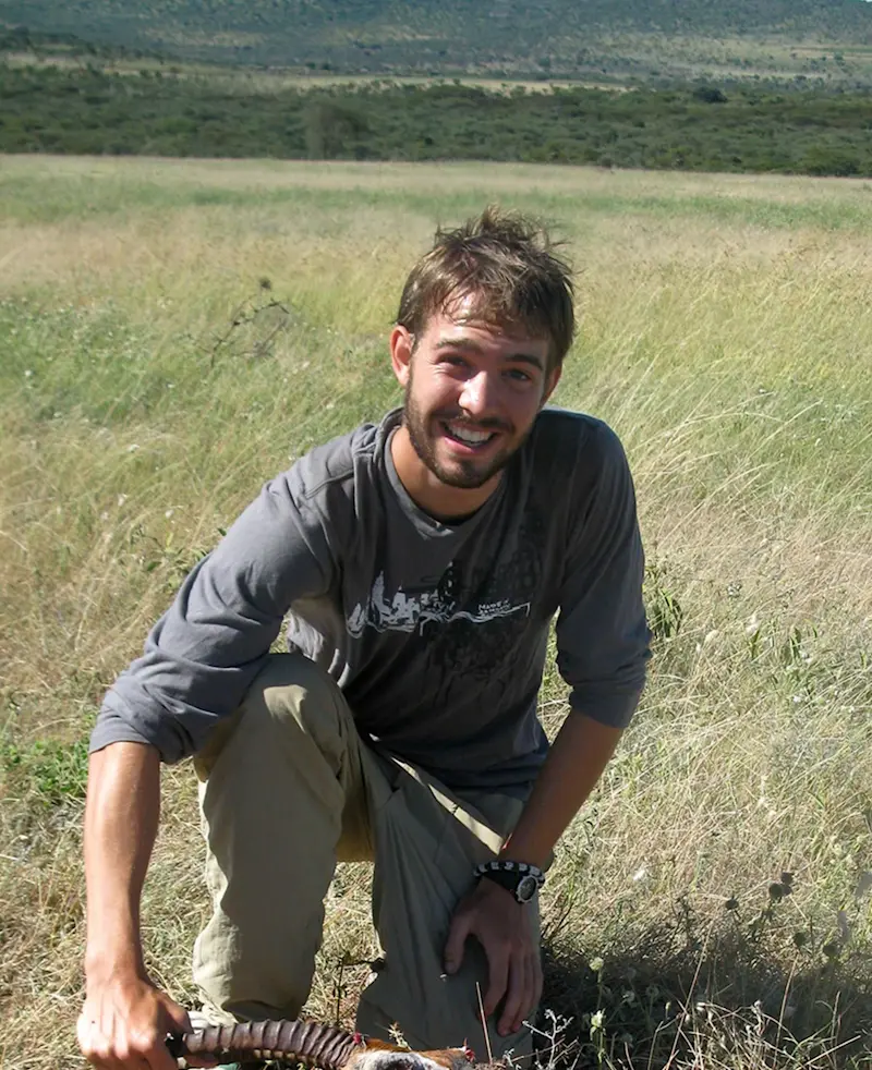 Smiling young man kneeling in tall grass on the plains