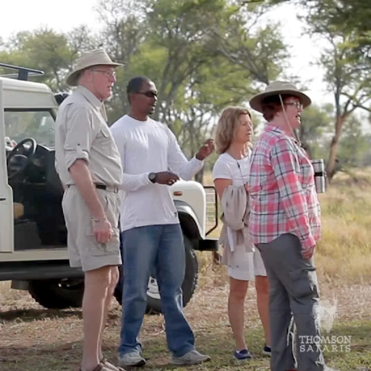 Safari guide James talking with travelers beside a safari vehicle