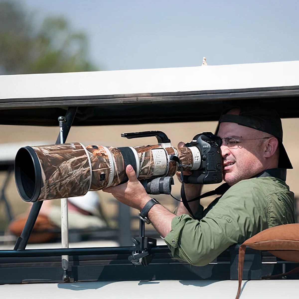 Portrait of photographer Wesley Bernard aiming a camera with a long lens from a safari vehicle