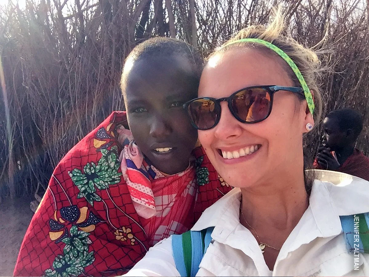 Smiling traveler taking a selfie with a young Maasai villager wrapped in a red patterned cloth