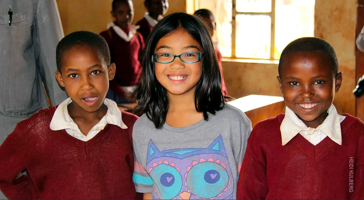 Smiling girl standing between two Tanzanian schoolchildren in red sweaters