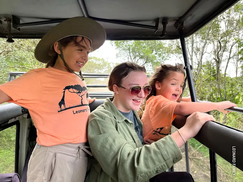 Excited children and a young woman looking out from an open safari vehicle