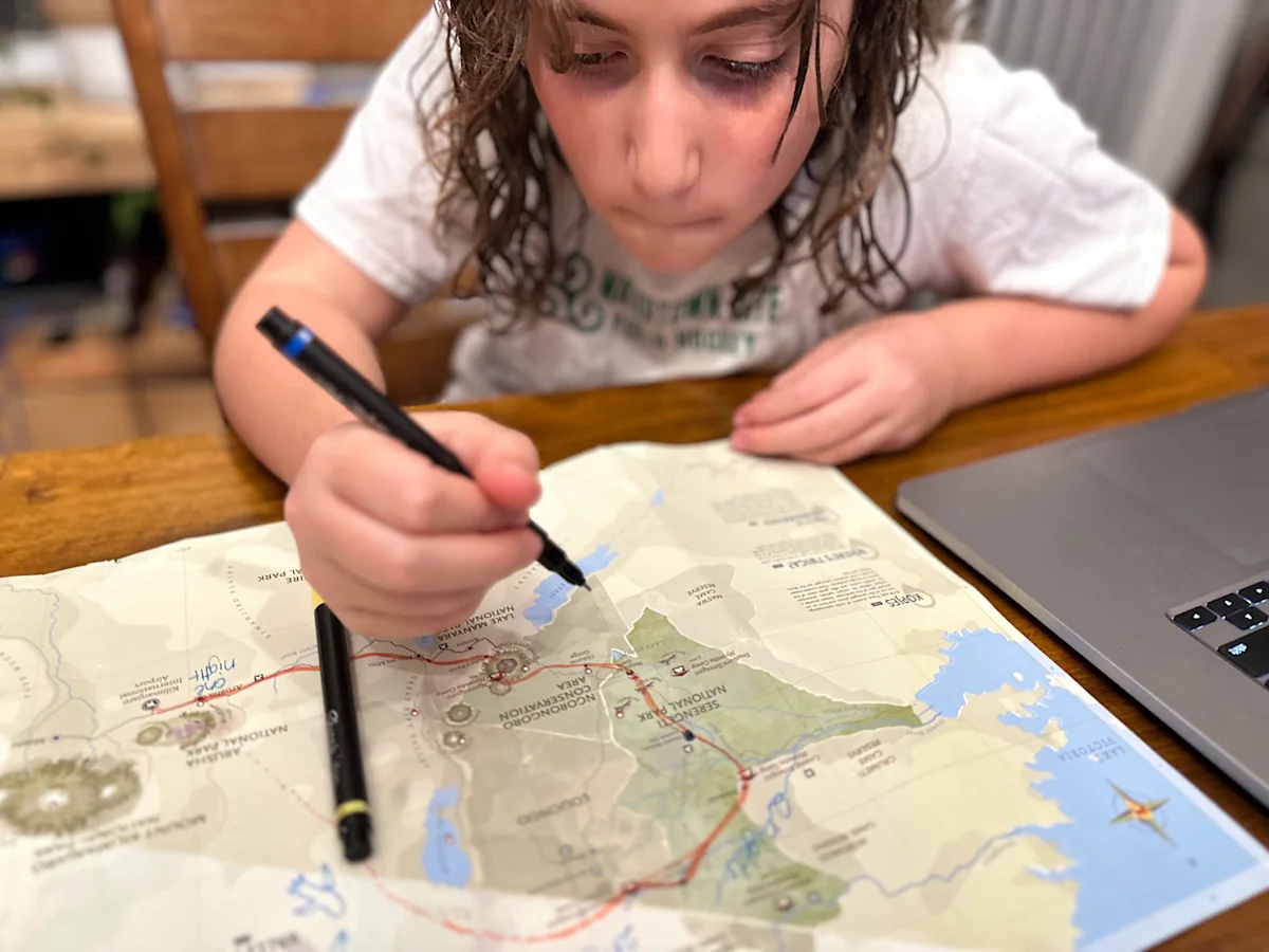 Child drawing a safari route on a printed map of Tanzania