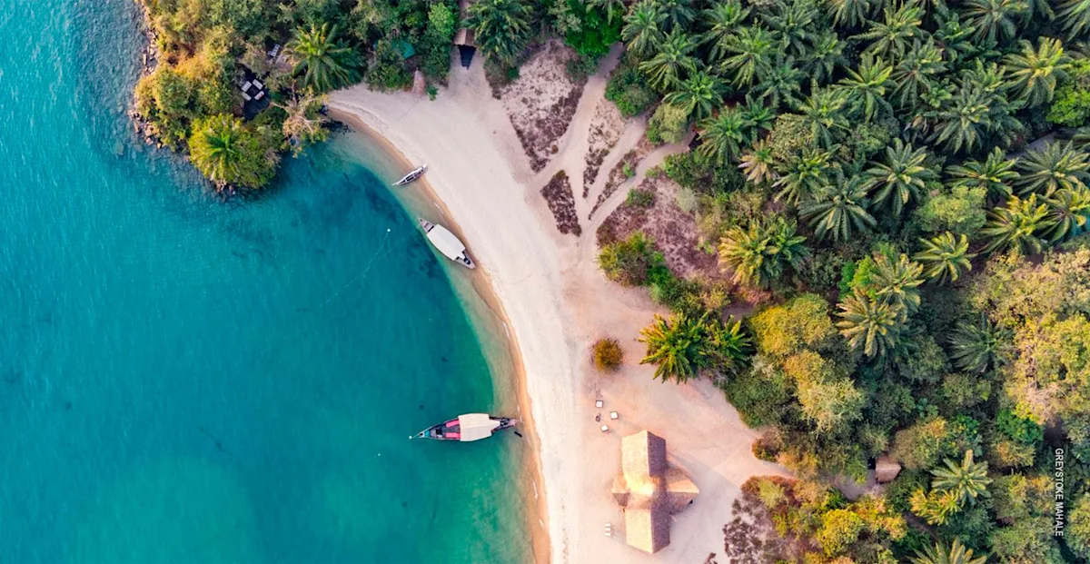 Aerial view of a sandy beach, boats, and palm forest at Greystoke Mahale on Lake Tanganyika