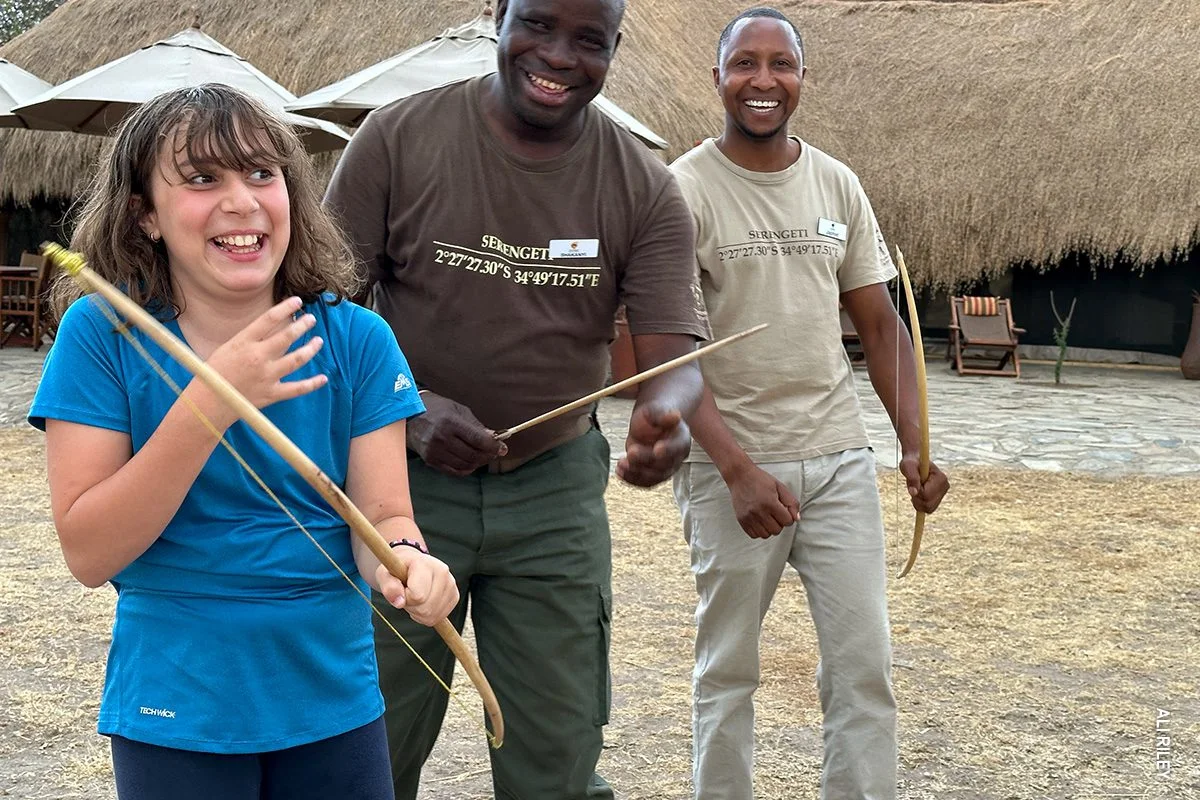 Laughing girl learning archery with a bow from two camp staff members