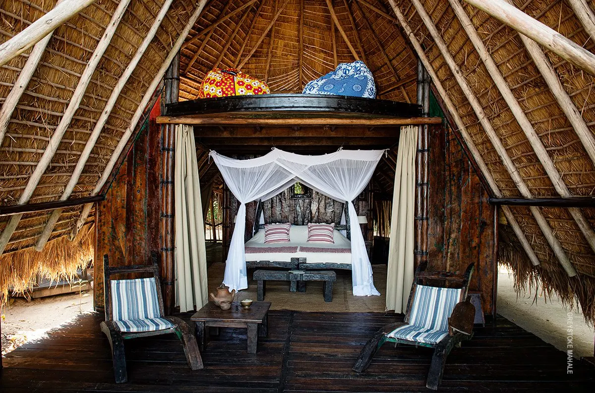 Thatched banda with a canopy bed and chairs at Greystoke Mahale