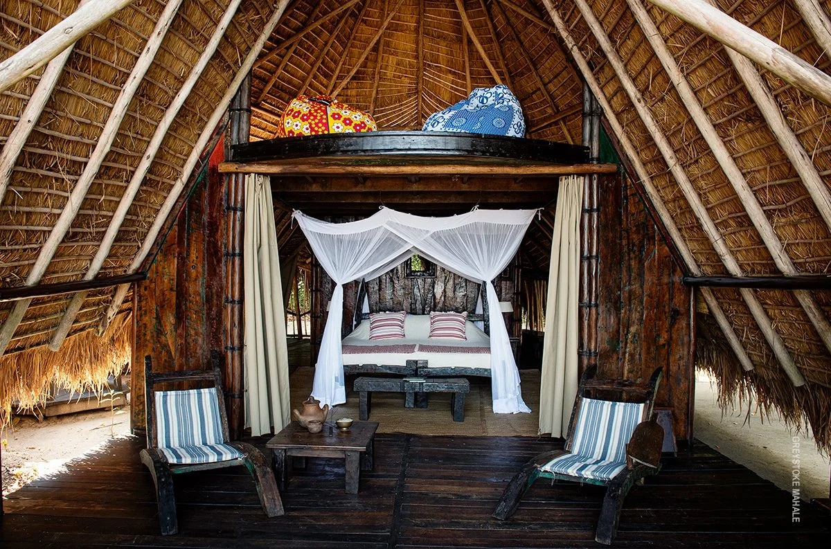 Thatched banda with a canopy bed and chairs at Greystoke Mahale