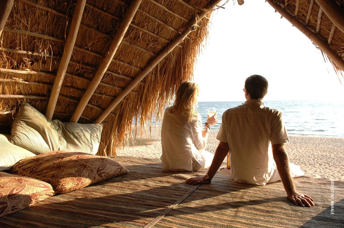 Couple relaxing under a thatched shelter looking out at the beach and lake