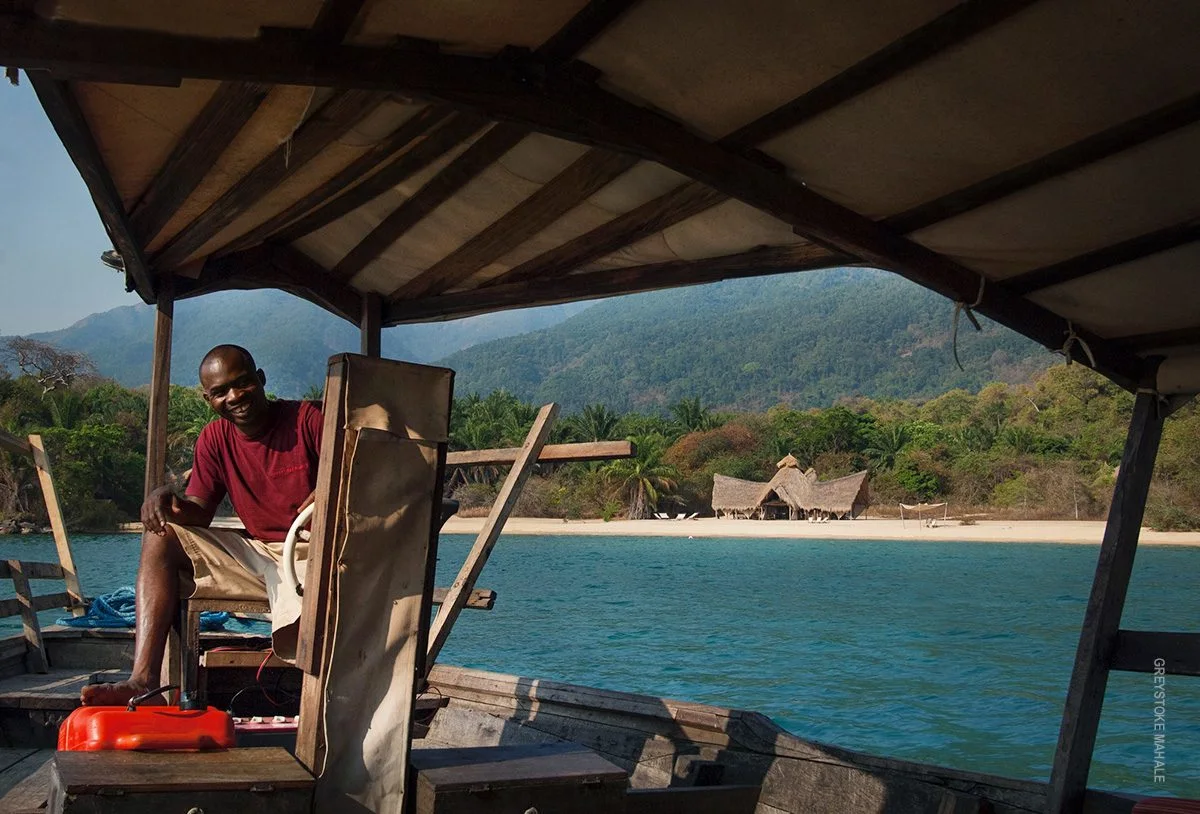 Smiling boat driver at the helm with a forested shore and lodge behind