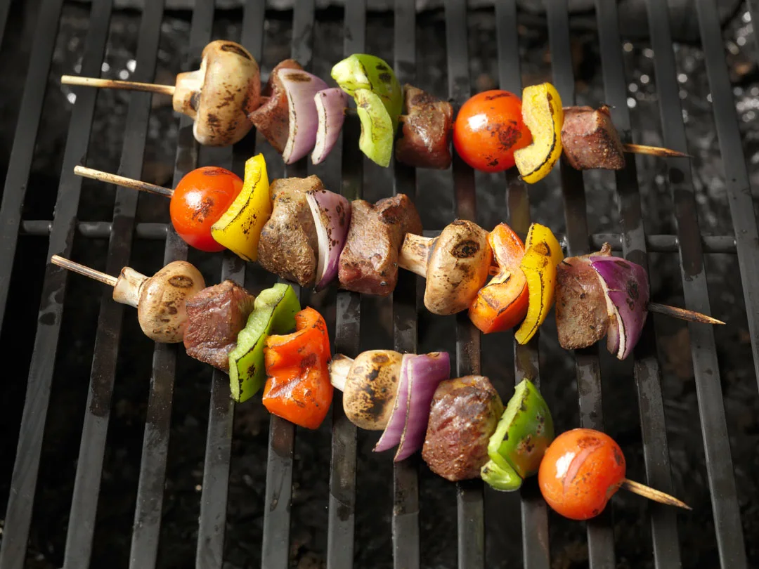 Skewers of meat, mushrooms, peppers, and tomatoes on a grill