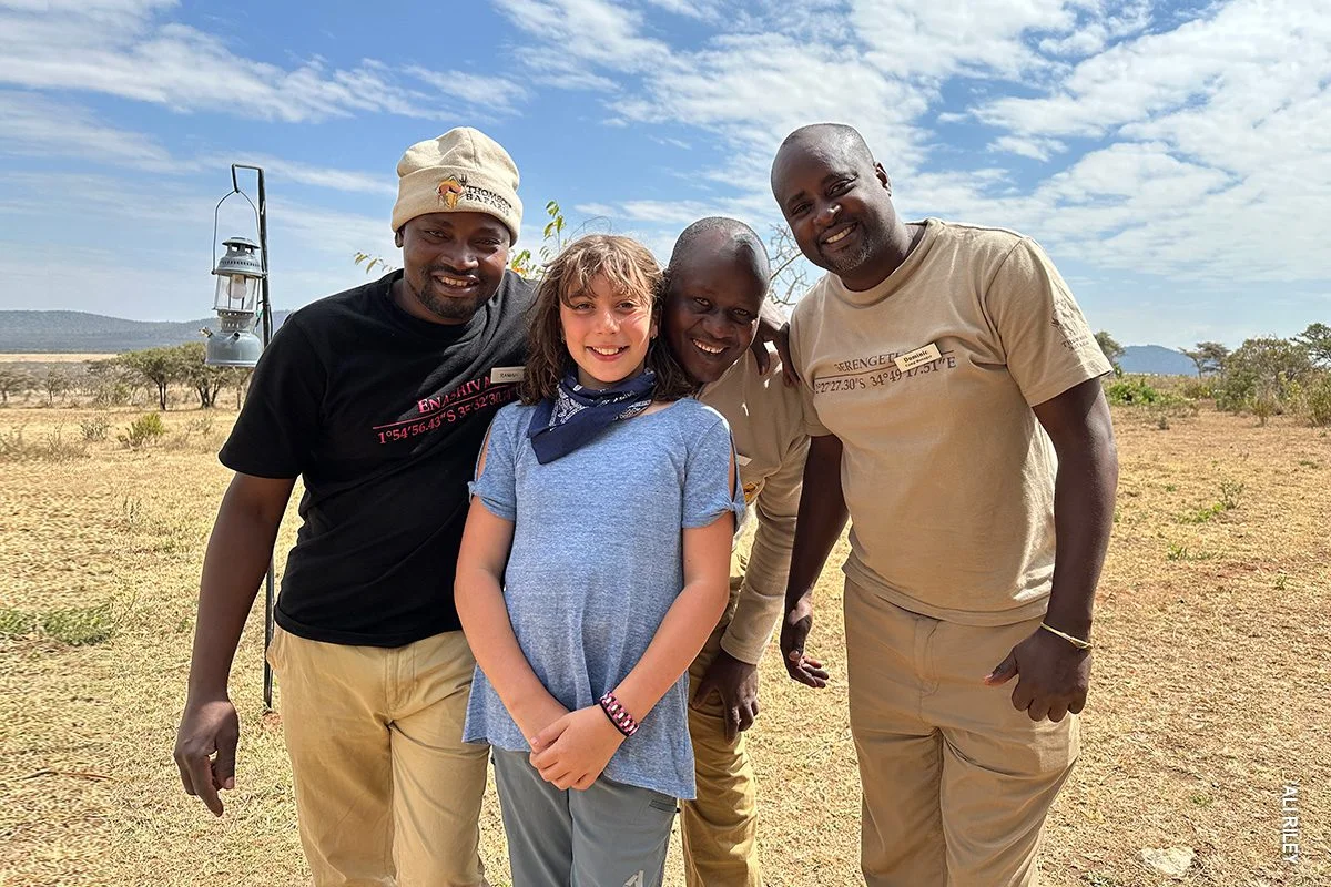 Girl posing with three smiling camp staff members on the plains