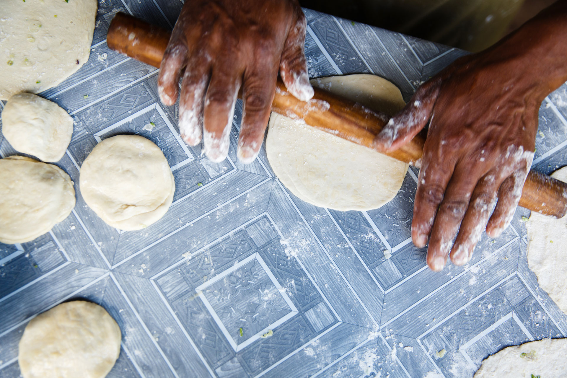 Hands rolling out chapati dough with a wooden rolling pin