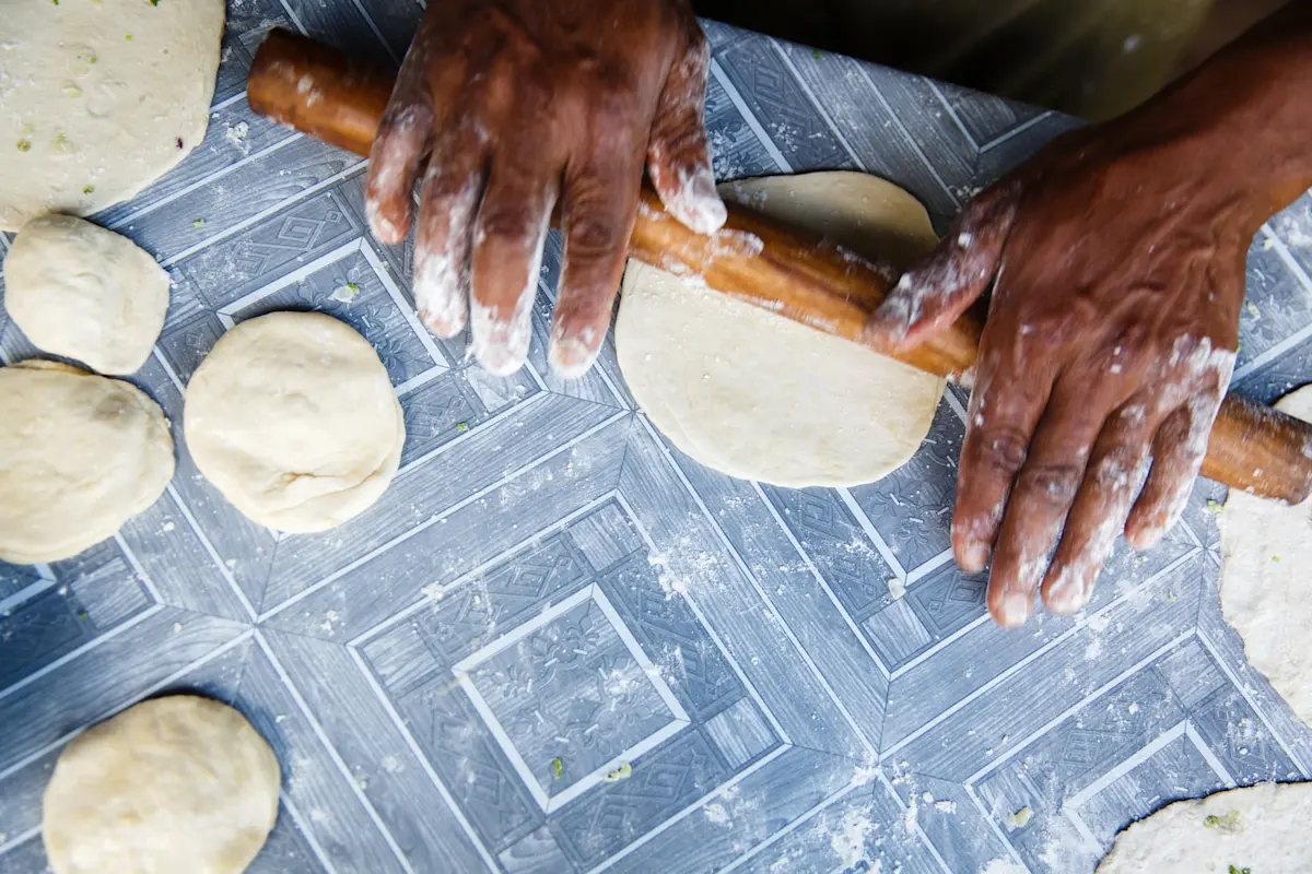 Hands rolling out chapati dough with a wooden rolling pin