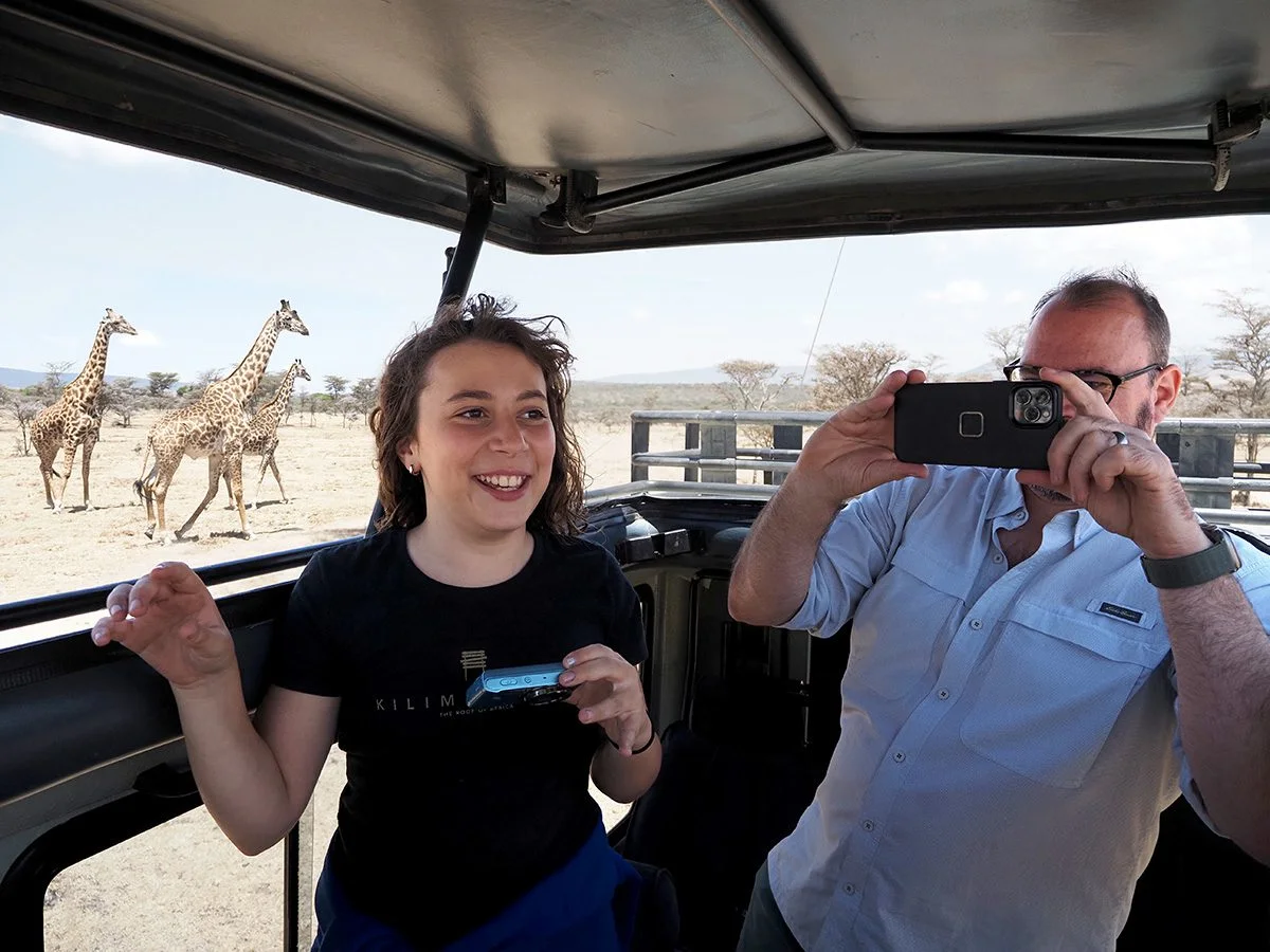 Girl and man in a safari vehicle watching and photographing giraffes