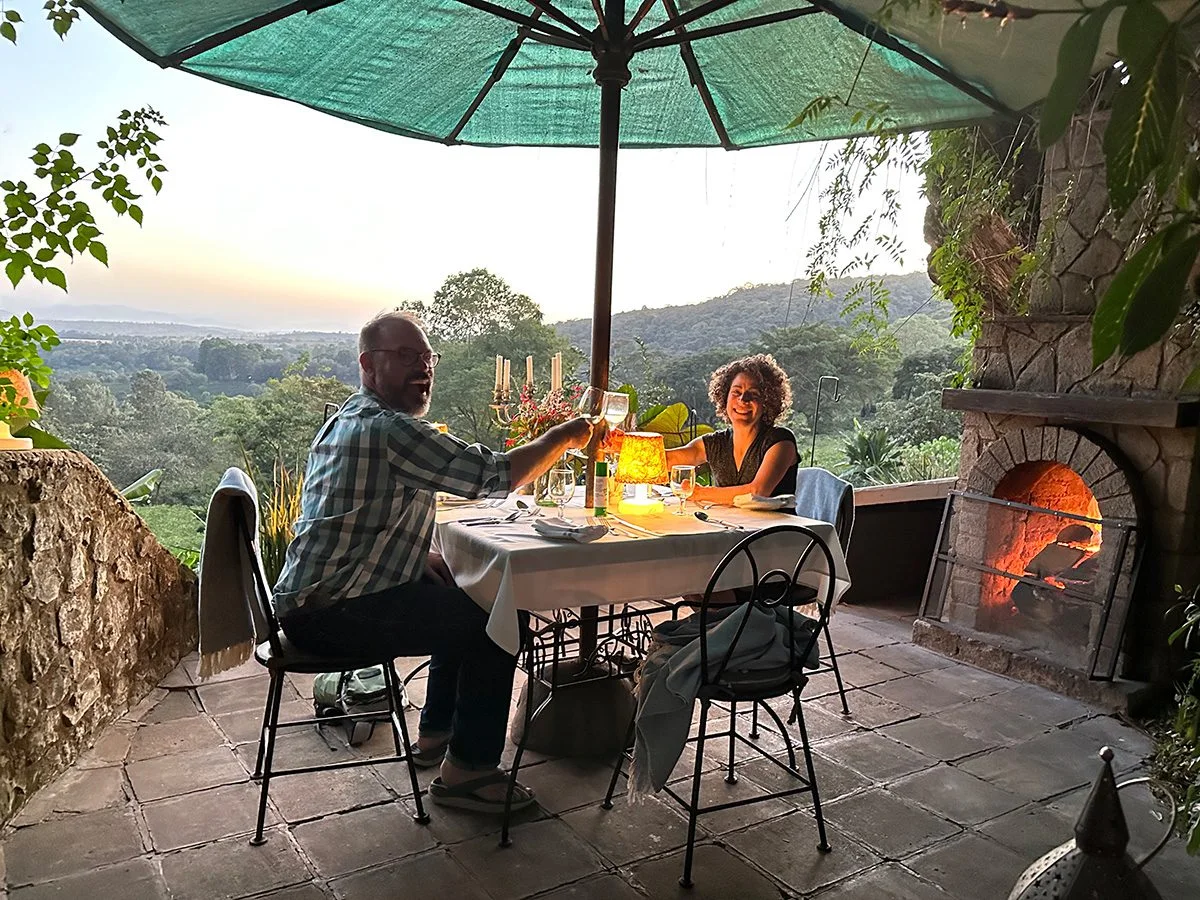 Couple dining by candlelight on a terrace overlooking green hills at sunset