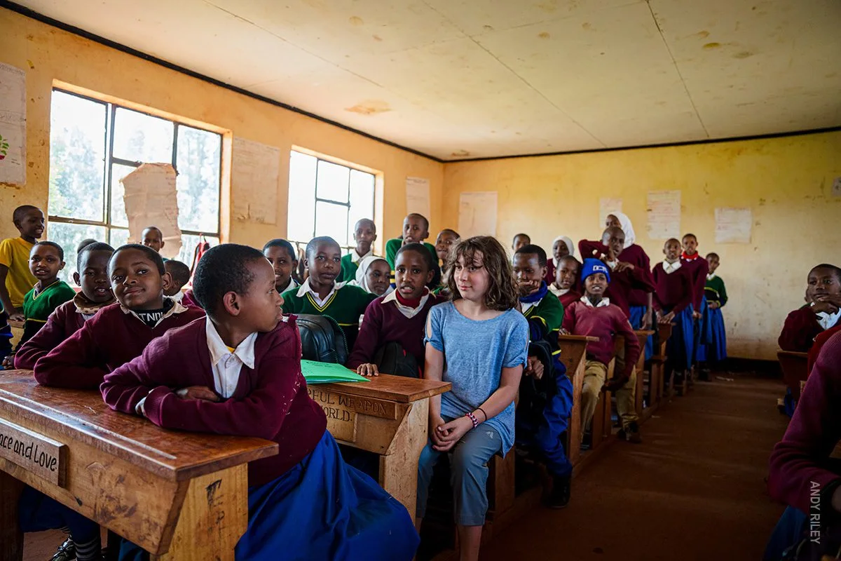 Visiting girl sitting among uniformed students at desks in a classroom