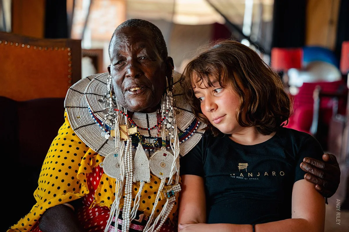Maasai woman in beaded jewelry with her arm around a young girl