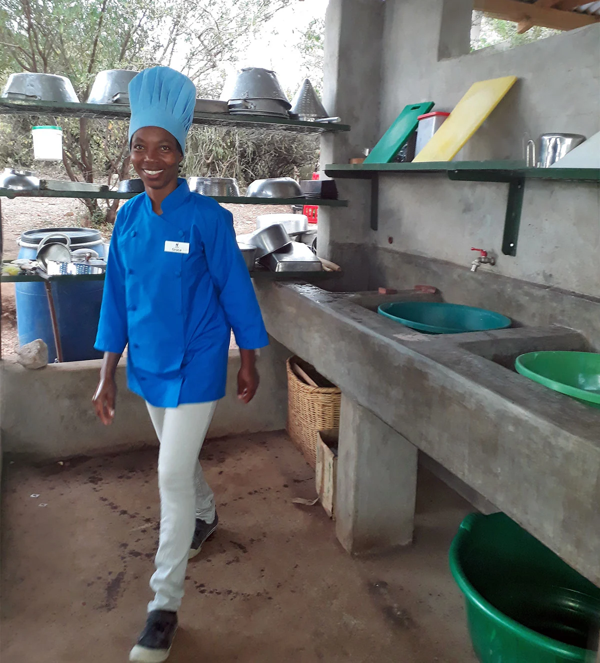 Grace, a trainee cook assistant, walking through the camp kitchen in a blue chef's uniform and hat