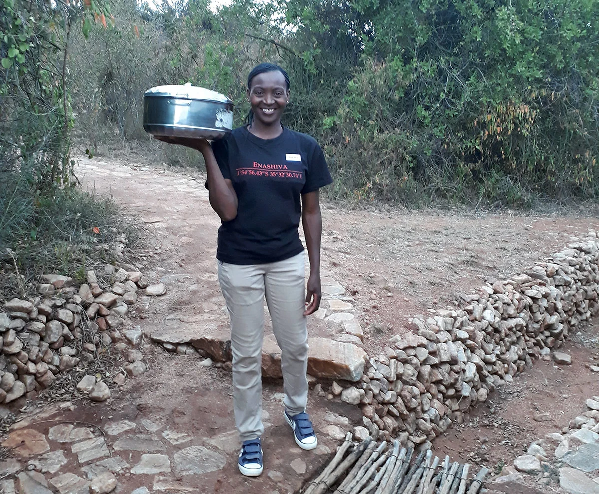 Neema, a trainee camp hand, holding a covered pot on a stone path