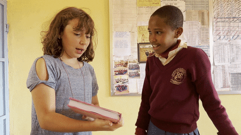 Visiting girl showing a book to a uniformed student in a classroom