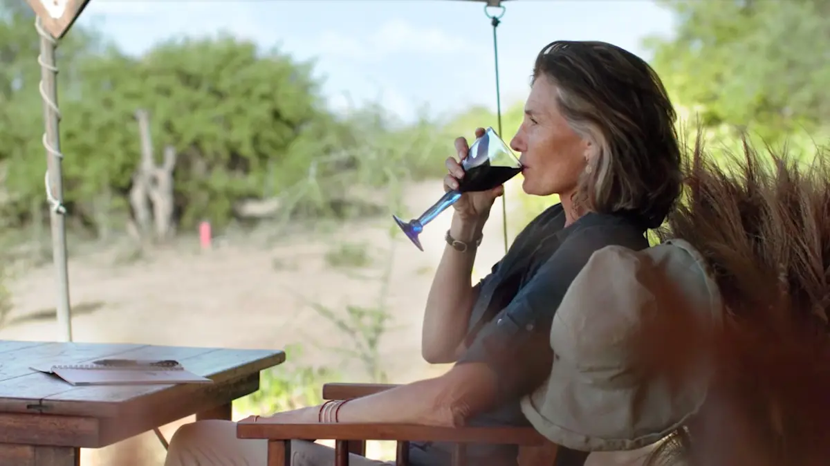 Woman sipping wine on a camp veranda overlooking the bush
