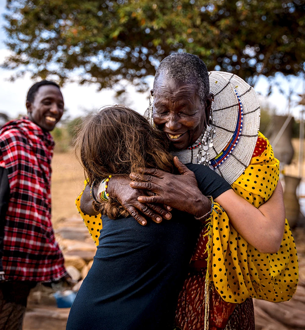 Maasai woman in beaded jewelry hugging a traveler